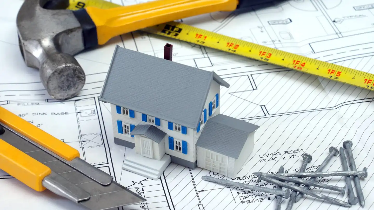 Building plans, a tape measure and hand tools on a drawing board