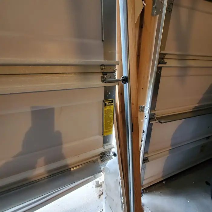 A garage door and jamb buckled by a vehicle impact