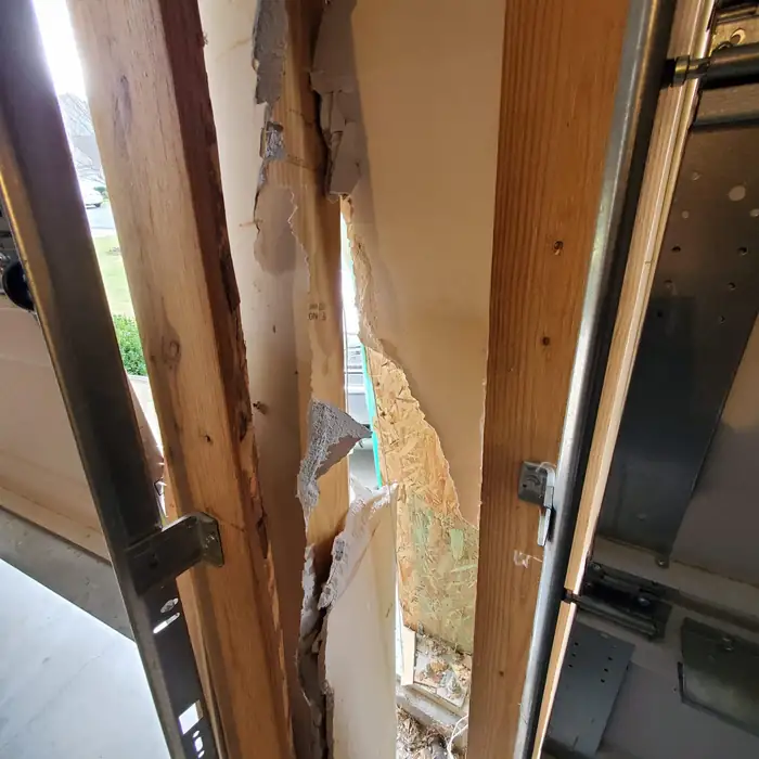 Torn drywall and splintered wall studs exposed after a vehicle struck the garage