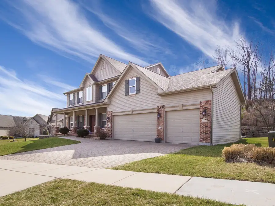 Two-storey beige-sided home with a front-facing three-car garage, brick accents and a paver driveway