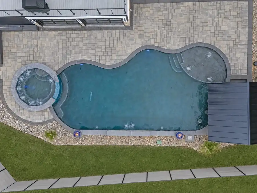 Overhead view of a freeform pool with a round spa and paver patio