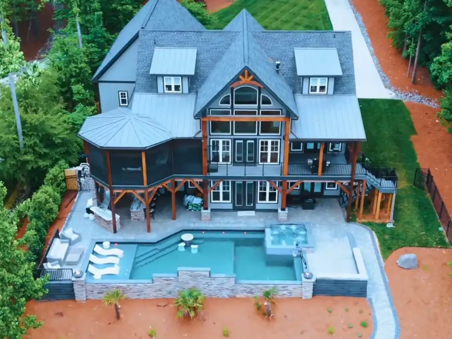 Aerial view of a lake house with a stone-walled pool, spa and covered patio