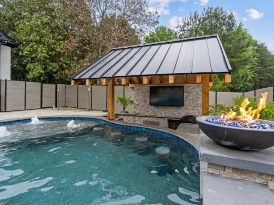 A freeform pool beside a covered pavilion with a stone TV wall and a fire bowl