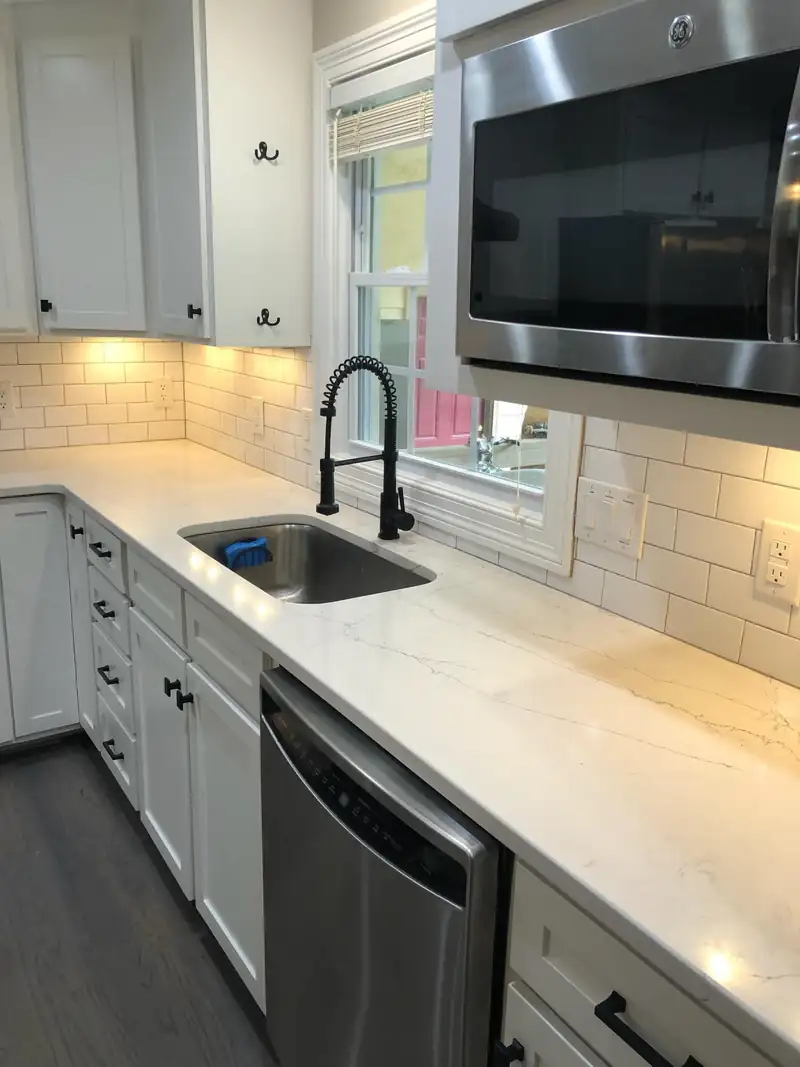 A renovated kitchen with white cabinets and quartz counters