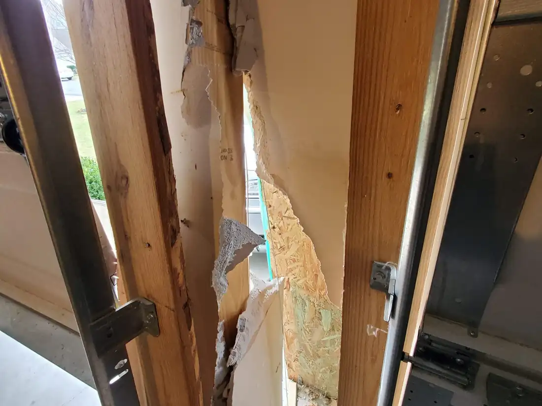 Splintered wall framing and torn drywall where a car struck the garage