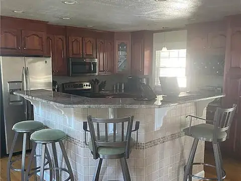 The original kitchen with dark cherry cabinets, a tiled peninsula and bar stools