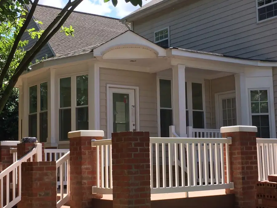 A covered front porch with white rails and brick piers